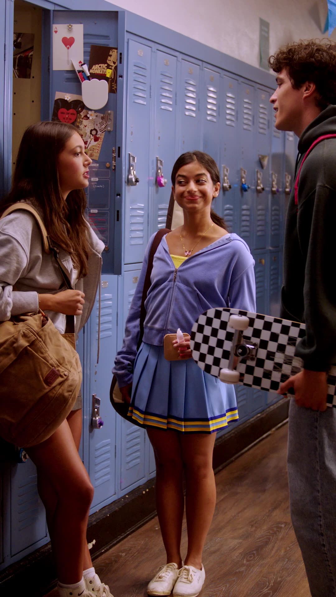 Strings Attached — three friends talking at their lockers, one holding a skateboard