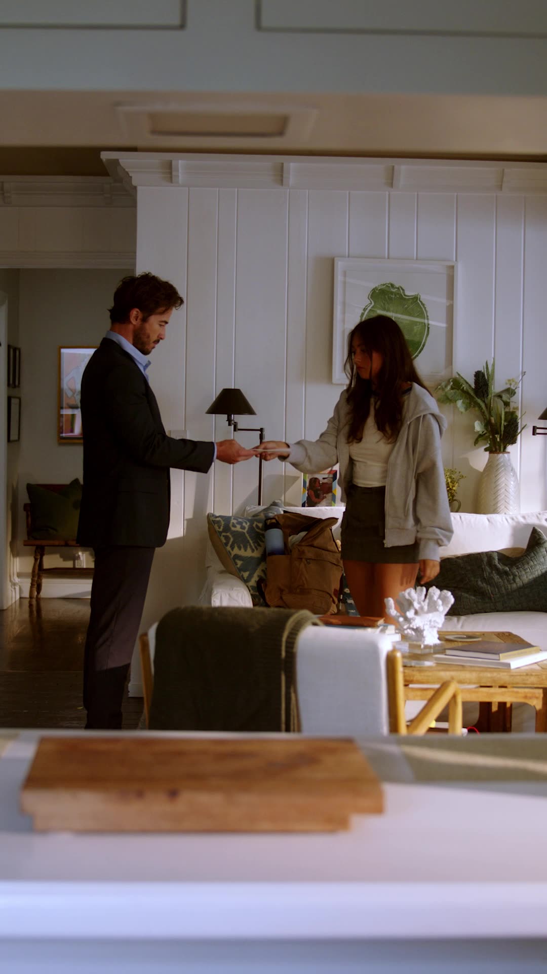 Strings Attached — a man in a suit handing an envelope to a young woman in a living room